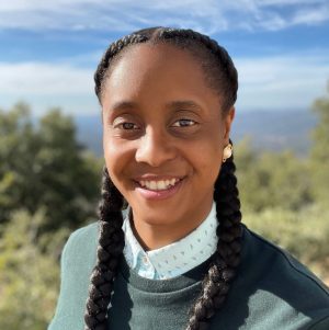 headshot of Jay Gash, a black queer person with two thick braids outdoors