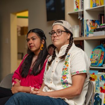 two Latinx folks sitting in front of a bookcase